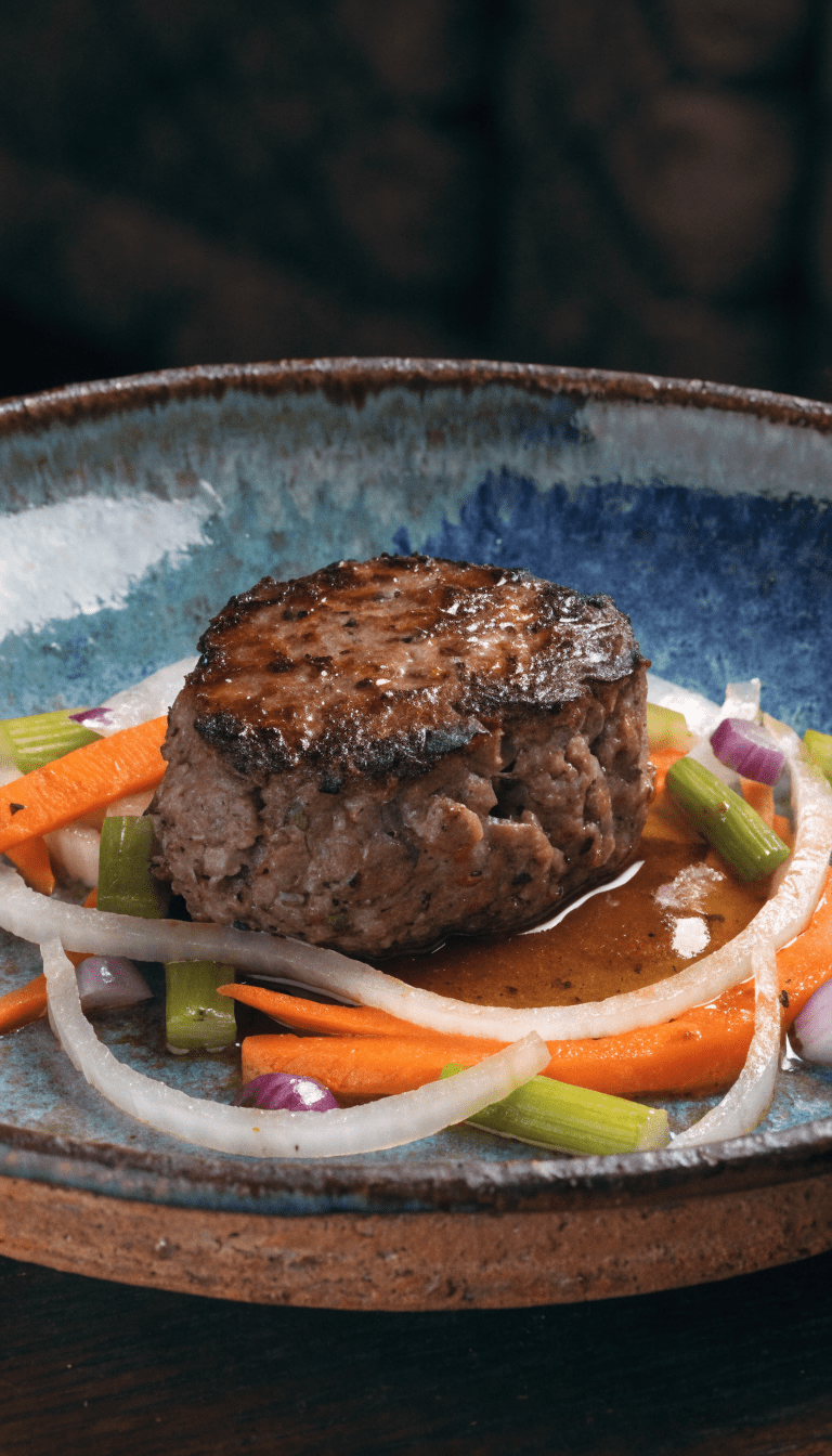 "Deer-meat patty on rustic plate with veg garnish"
